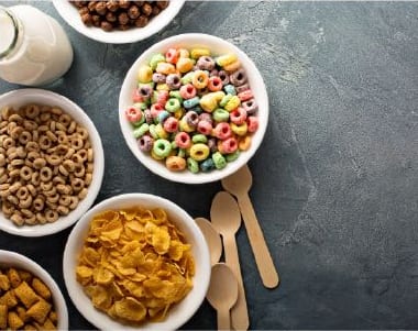 Five bowls of breakfast cereal with wooden spoons on gray slate table