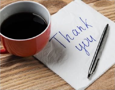 "Thank you" written on white napkin, next to cup of coffee and silver pen