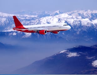 Red and white airplane flying over snowy mountains